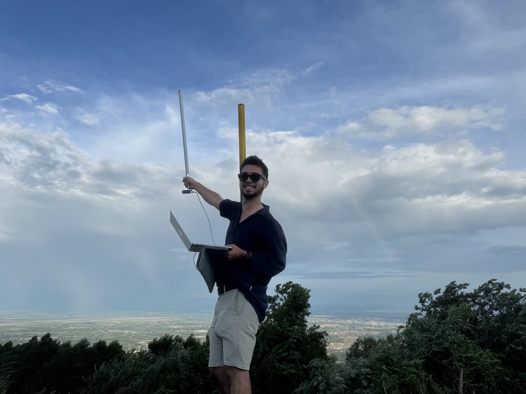 Me on Mount Cavallo, holding up the antenna of the receiving node with a laptop in the other hand, the plain far below