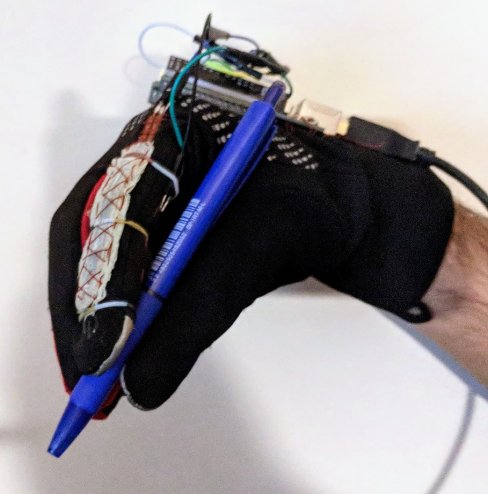The instrumented glove, worn while holding a pen, with a flex sensor stitched along the finger